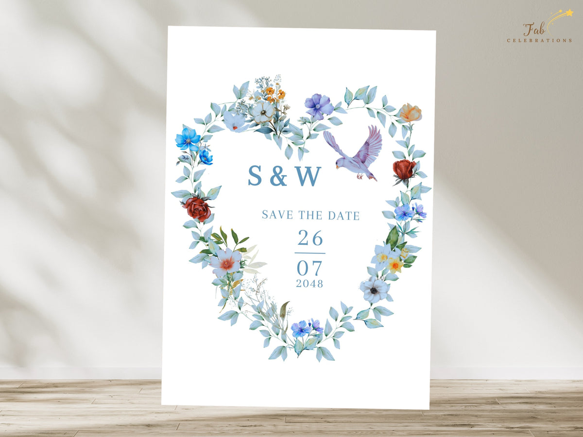 Coordinated wedding save the date template featuring a watercolor-inspired floral heart wreath with blue flowers, green foliage and two doves surrounding the couple's initials and wedding date.