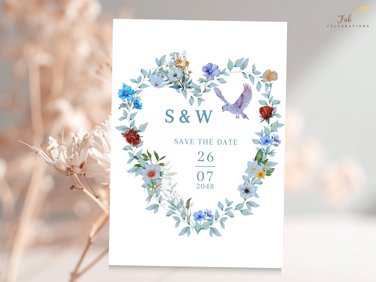 Save the date card featuring a watercolor-inspired floral heart wreath with soft blue flowers, green botanical accents and two doves around the couple's initials, wedding date and year.