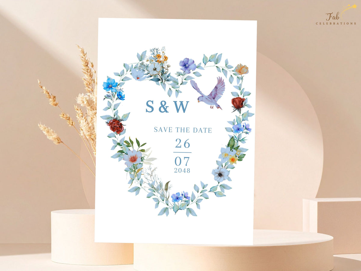 Save the date card featuring the couple's initials and wedding date inside a watercolor-inspired heart wreath with dusty blue flowers, greenery and two doves for a coordinated wedding announcement.
