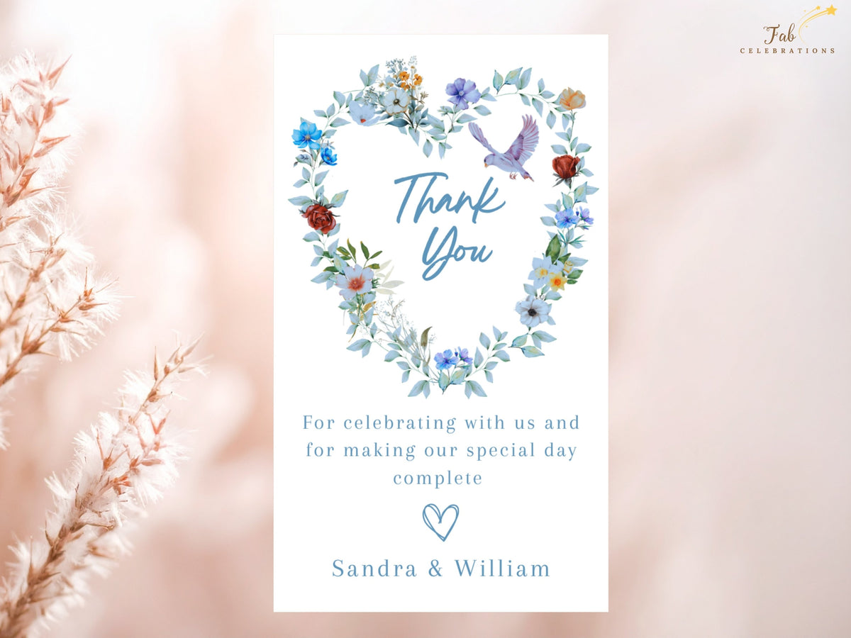 Wedding thank you card featuring a watercolor-inspired floral heart wreath with dusty blue flowers, greenery and a dove above an elegant gratitude message and the couple's names.