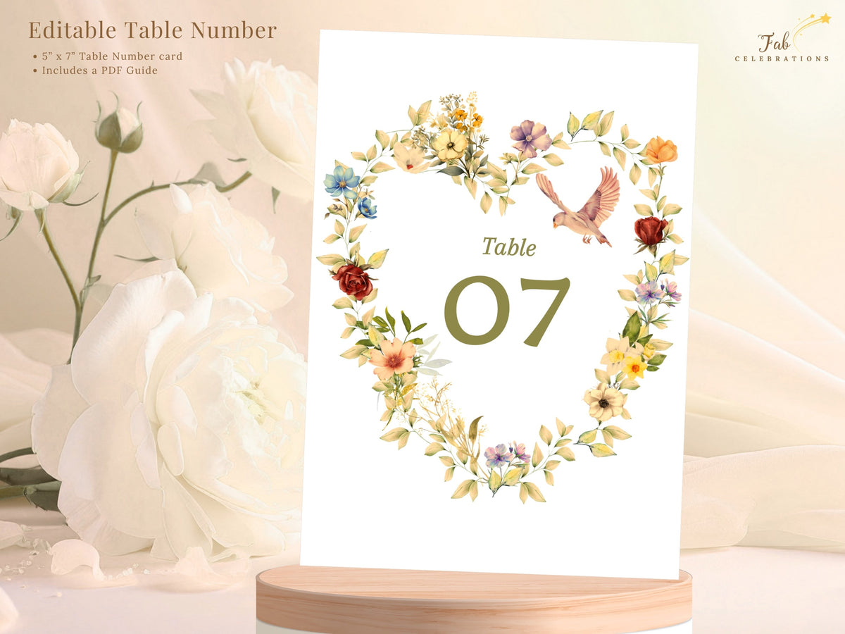Editable romantic wedding table number shown with a floral heart and dove design, soft golden and blush flowers, sage greenery, and customizable numbering in a Canva template for receptions.