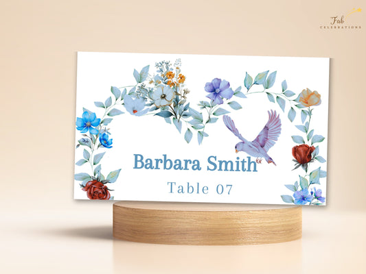 Elegant Table Name Card featuring a guest name and table number framed by watercolor-inspired blue flowers, green foliage and a graceful dove for coordinated wedding reception place settings.