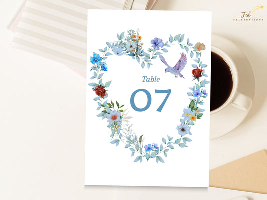 Elegant Wedding Table Number Card featuring a large blue table number framed by a watercolor-inspired heart wreath with blue flowers, green foliage and a graceful dove for coordinated reception decor.