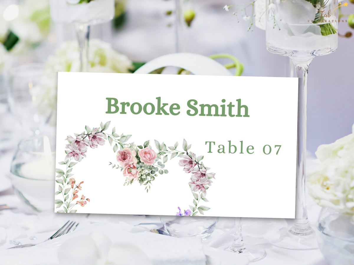 Wedding place card featuring the guest name and table assignment with a delicate watercolor-inspired floral arrangement of pink roses, purple blossoms and green botanical accents.