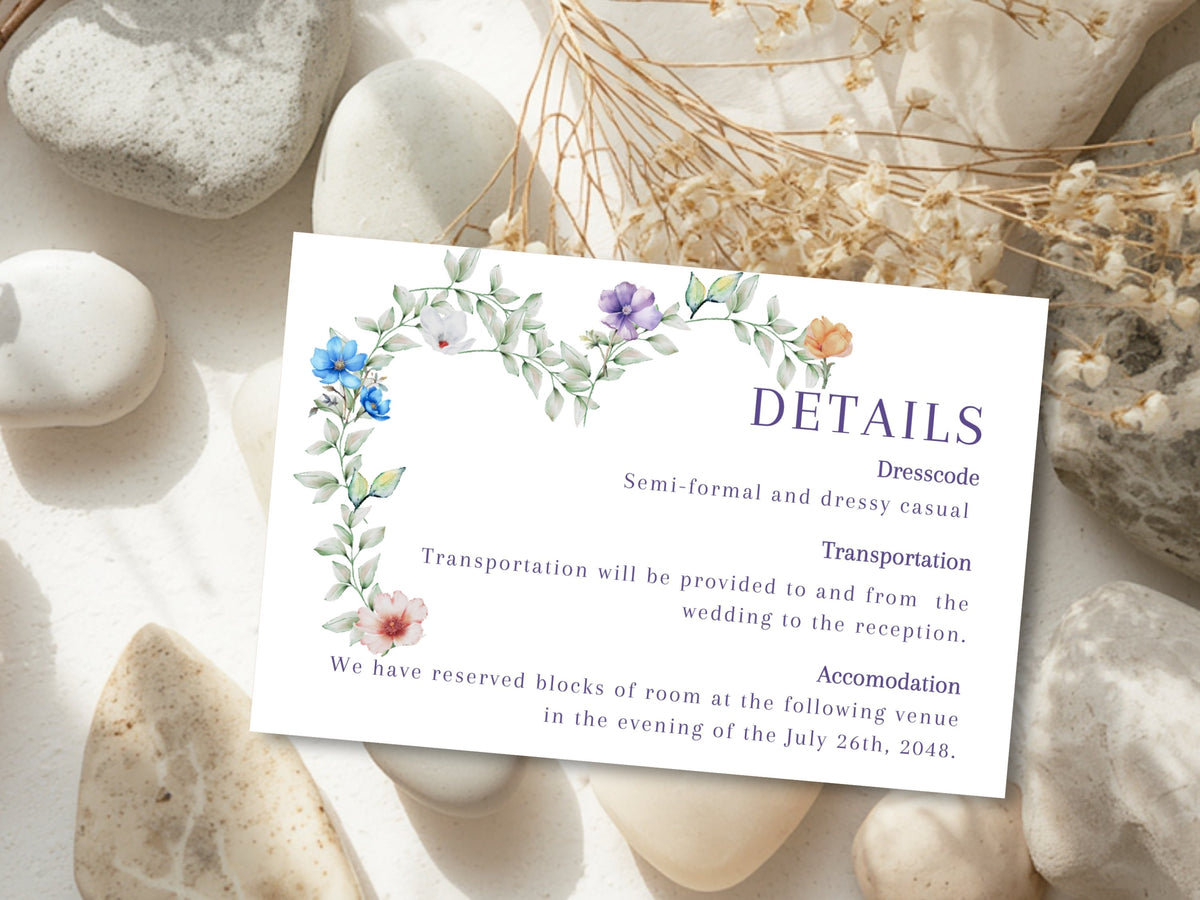 Wedding details card with travel, transportation and accommodation information, decorated with watercolor-inspired green foliage and delicate blue, purple, white and peach flowers in a romantic heart motif.