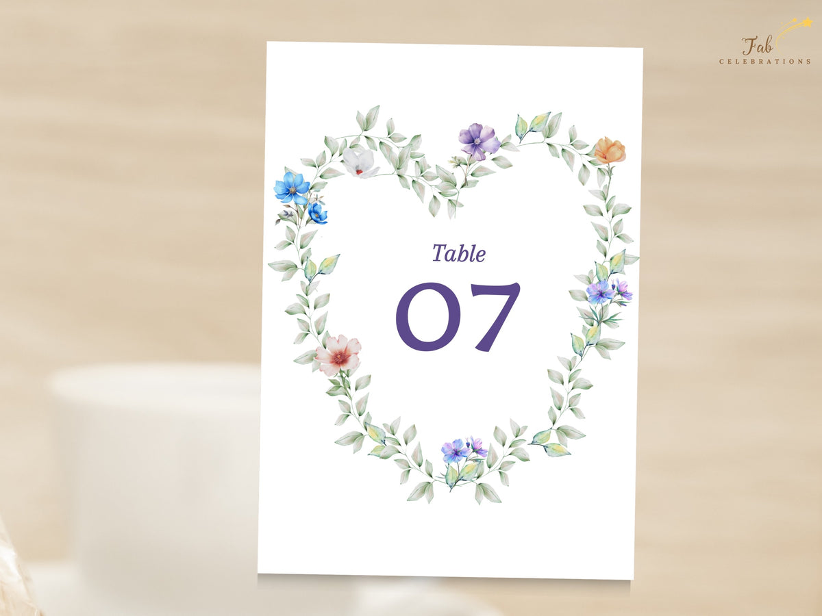 Wedding table number featuring airy watercolor-inspired greenery and delicate pastel garden flowers arranged in a wreath around a prominent purple table number for coordinated wedding decor.