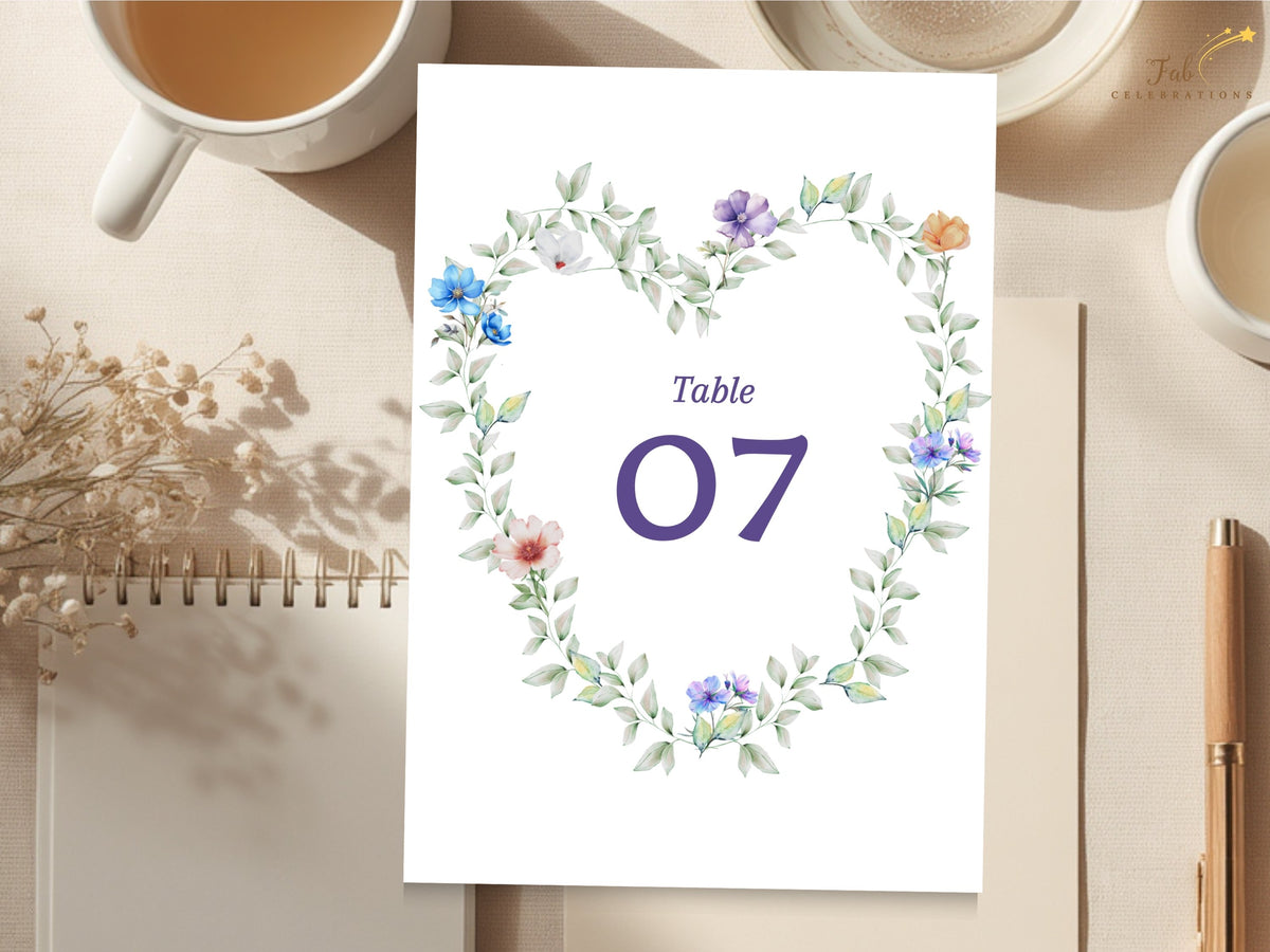 Wedding table number card featuring a watercolor-inspired wreath of airy greenery and delicate pastel flowers surrounding a large purple number for a romantic coordinated reception display.