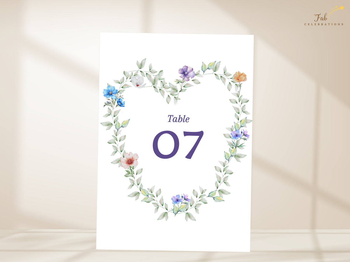 Wedding table card with a large purple table number framed by a watercolor-inspired wreath of soft pastel flowers and airy greenery, designed to coordinate with romantic wedding stationery.