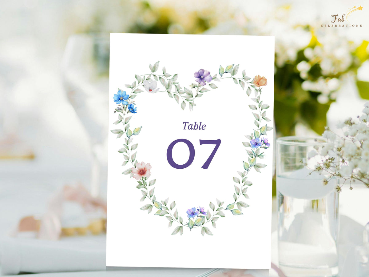 Pastel Garden Table Number card featuring a watercolor-inspired botanical wreath of delicate pastel flowers and airy greenery surrounding a prominent purple table number for wedding reception seating.