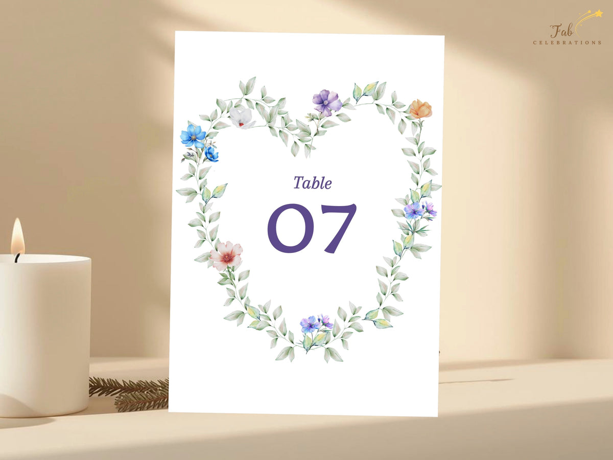 Wedding reception table number featuring a romantic watercolor-inspired botanical wreath with delicate pastel flowers and a large elegant purple number centered inside the floral design.