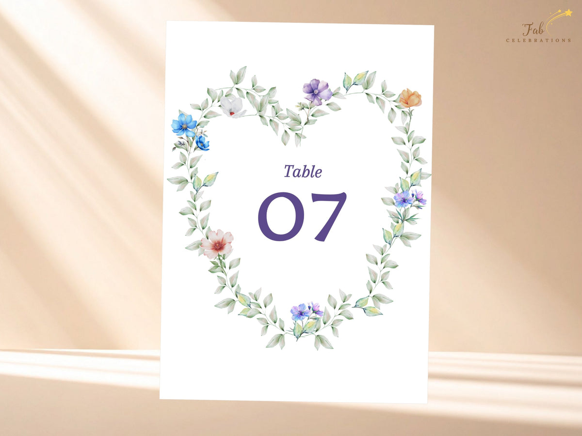 Wedding table number card featuring a watercolor-inspired floral wreath with airy green foliage and delicate multicolor flowers surrounding a large elegant purple number for reception seating.