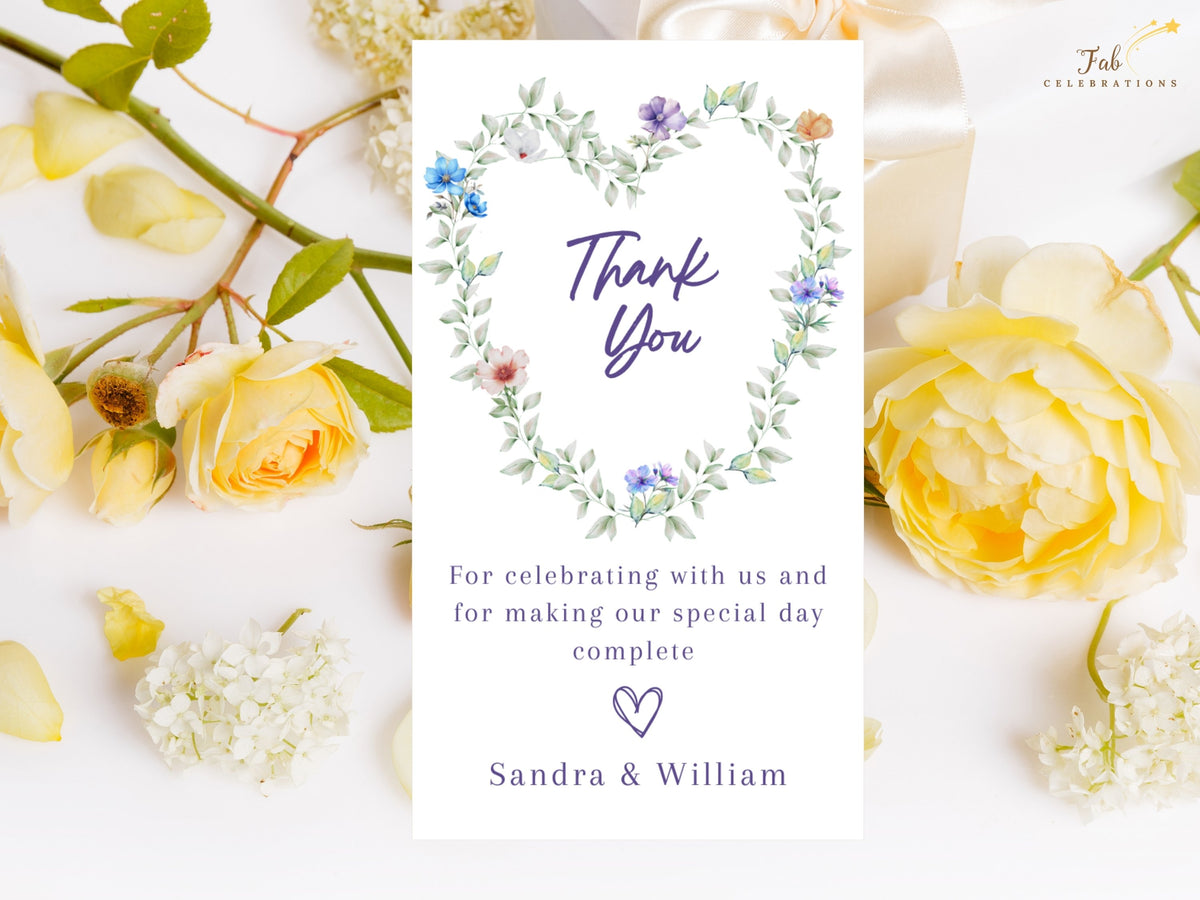 Pastel Wedding Thank You Card featuring a watercolor-inspired heart-shaped wreath of airy green foliage and delicate blue, purple, white, peach and pink flowers around elegant purple thank you lettering and a personalized gratitude message.