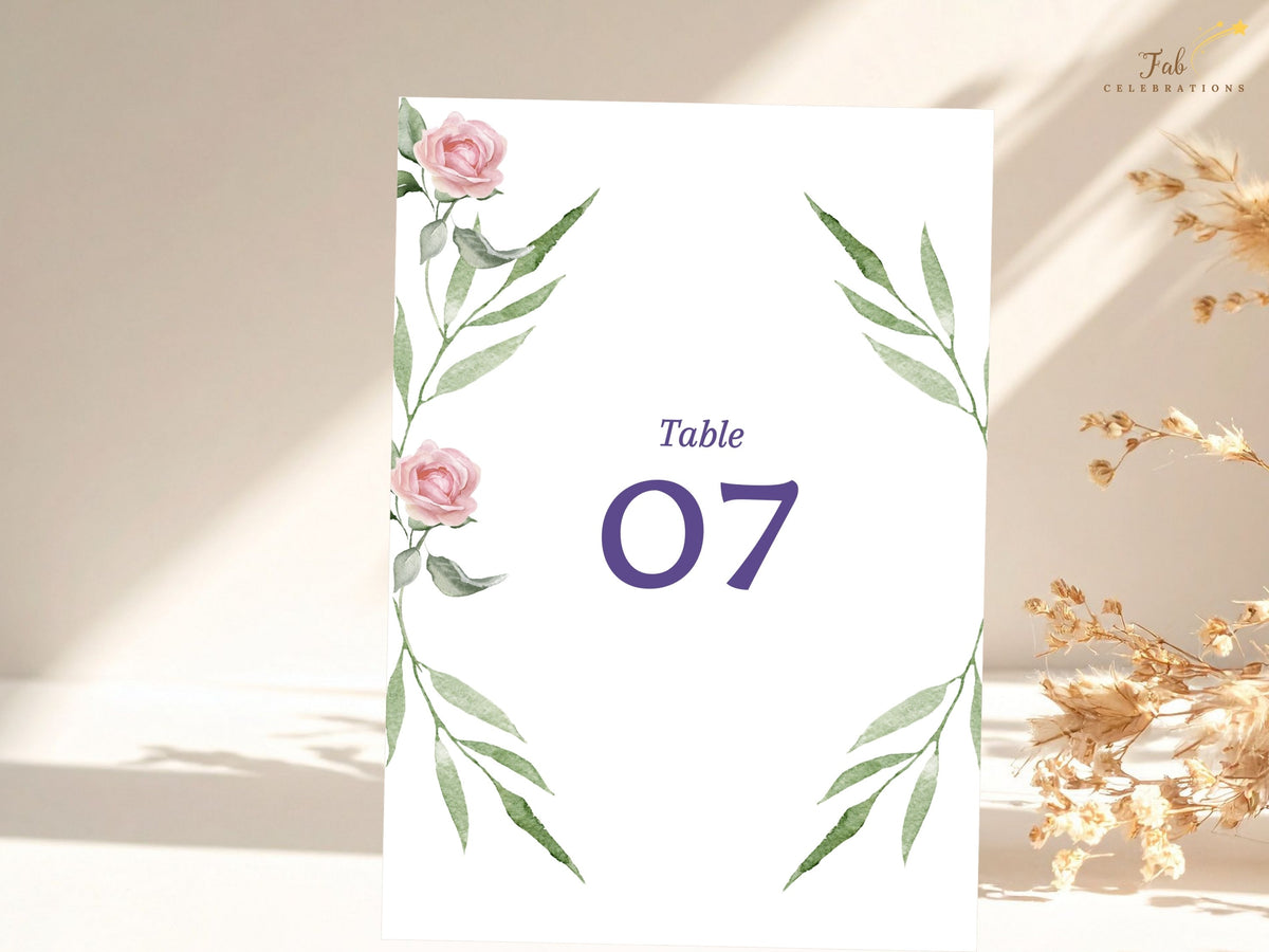 Botanical table number card featuring watercolor-inspired blush pink roses and green leafy branches framing a prominent purple number for clear and romantic wedding table identification.