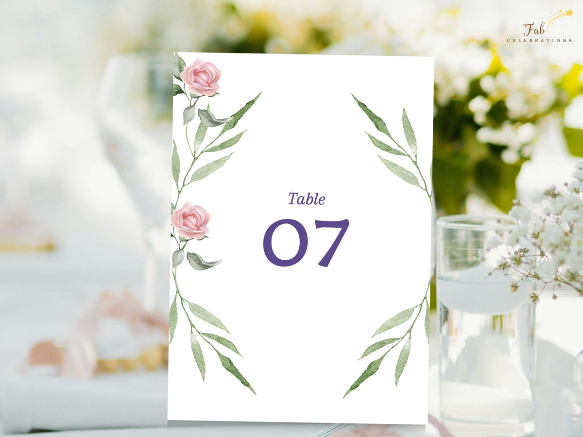 Wedding table number card decorated with watercolor-inspired blush roses and airy green foliage, with refined purple lettering and a prominent number for coordinated reception tables.
