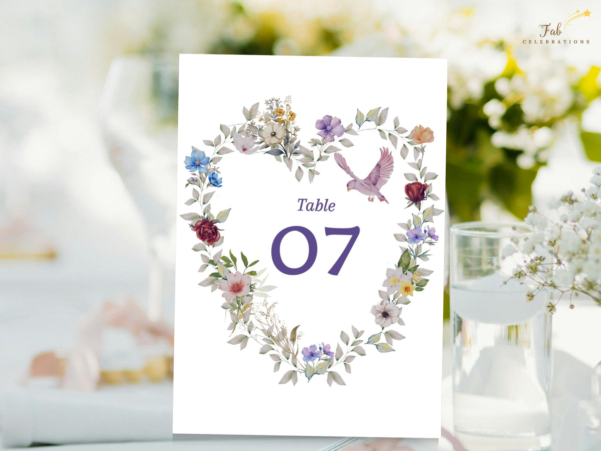 Wedding table number card featuring a large purple seven within a watercolor-inspired botanical heart of colorful garden flowers and a small dove above the numeral. Editable in Canva.