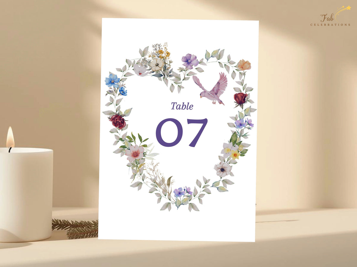 Wedding reception table number seven with watercolor-inspired flowers arranged in a romantic heart wreath, soft foliage and a dove above the large purple numeral. Editable in Canva.