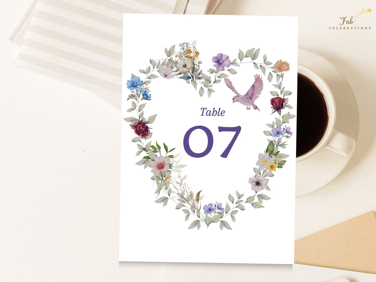 Purple floral wedding table number with an editable number seven framed by a watercolor-inspired heart wreath of violet, blue and pink blooms, accented with a delicate dove. Editable in Canva.