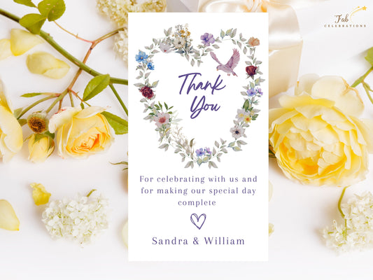 Purple Floral Wedding Thank You Card with purple script lettering, a watercolor-inspired floral heart of blue, pink and violet blooms, and a small dove above a warm message signed by the couple.