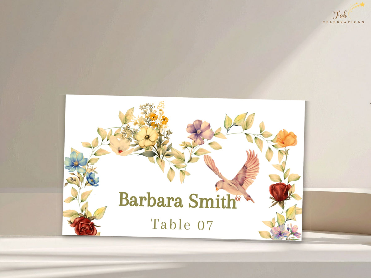 Ivory romantic wedding name card featuring a personalized guest name and table number beneath watercolor-inspired golden florals, pink blooms, delicate greenery, and a charming dove.
