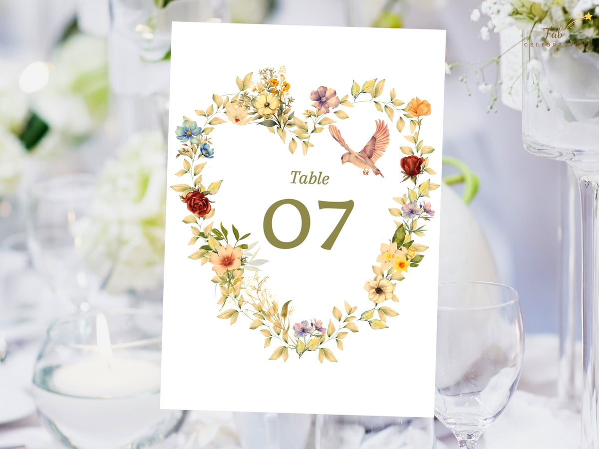 Wedding reception table number with a romantic floral heart wreath, two soft doves, pastel blooms, and sage leaves surrounding an editable olive green table 07 in a printable Canva design.