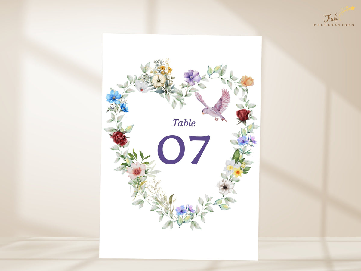 Floral reception table number card featuring a watercolor-inspired heart-shaped arrangement of colorful blossoms, delicate greenery and a graceful dove surrounding table number 07.
