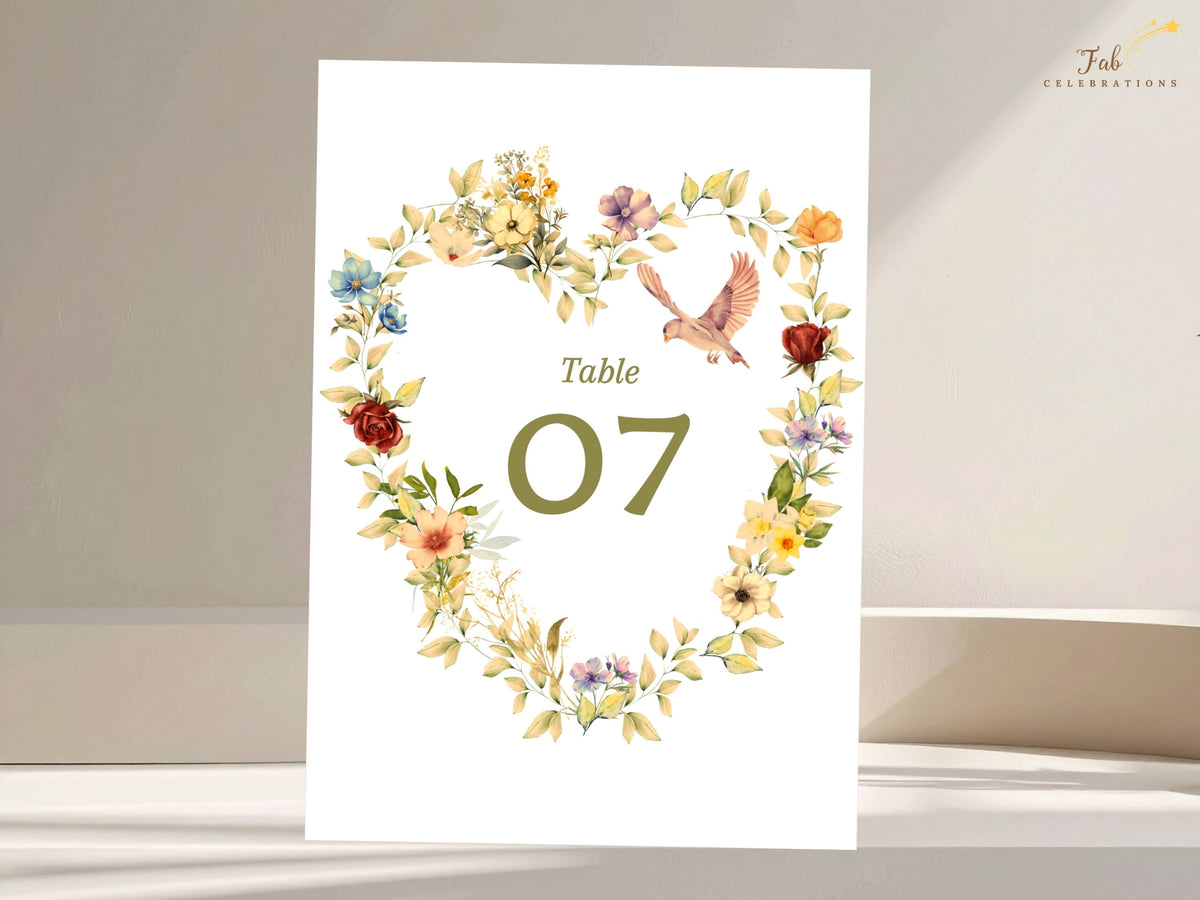 Watercolor-inspired floral heart wedding table number card with delicate dove accents, warm yellow and pink flowers, sage foliage, and editable table numbering for romantic reception decor.