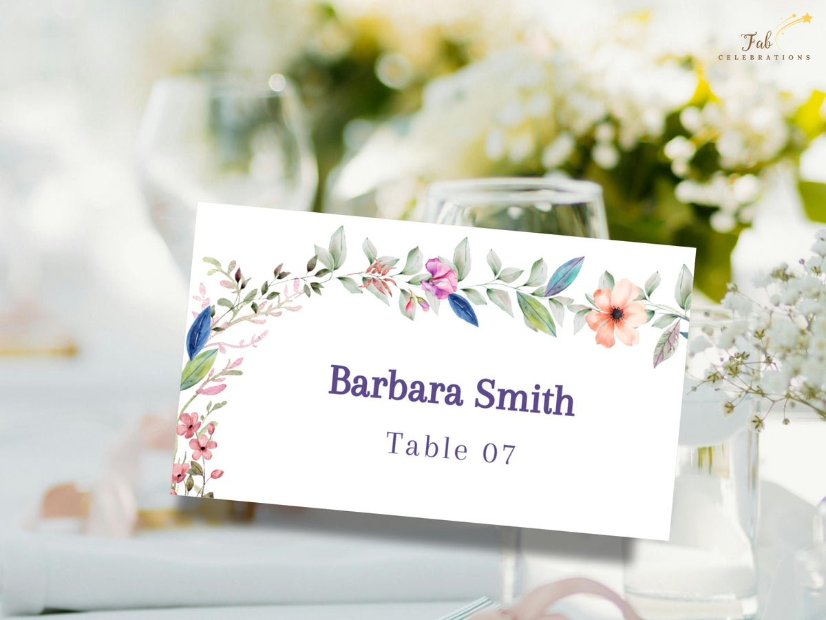Floral reception name card with watercolor-inspired blossoms and greenery framing a personalized guest name and table assignment for wedding seating.