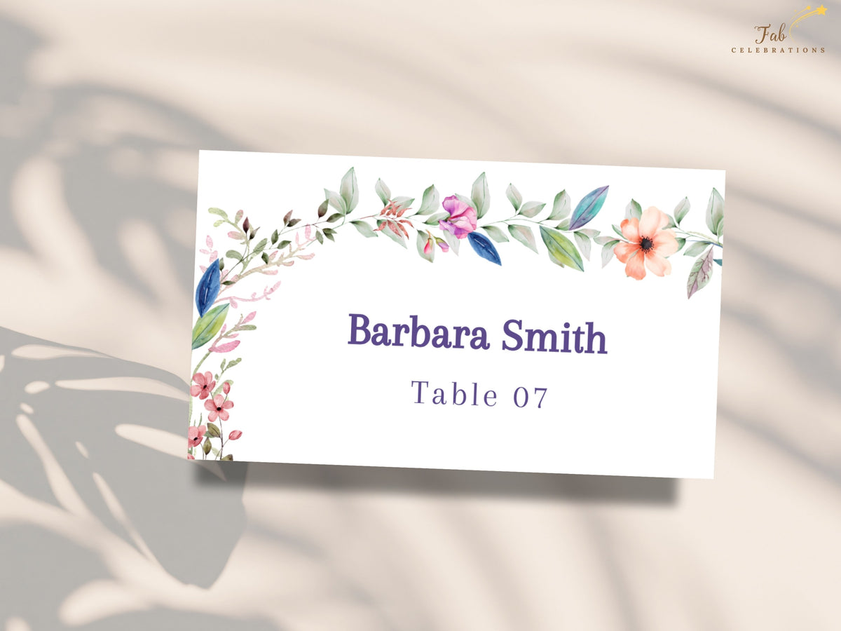 Printable floral wedding name card with watercolor-inspired blossoms and greenery surrounding a customizable guest name and assigned table number.