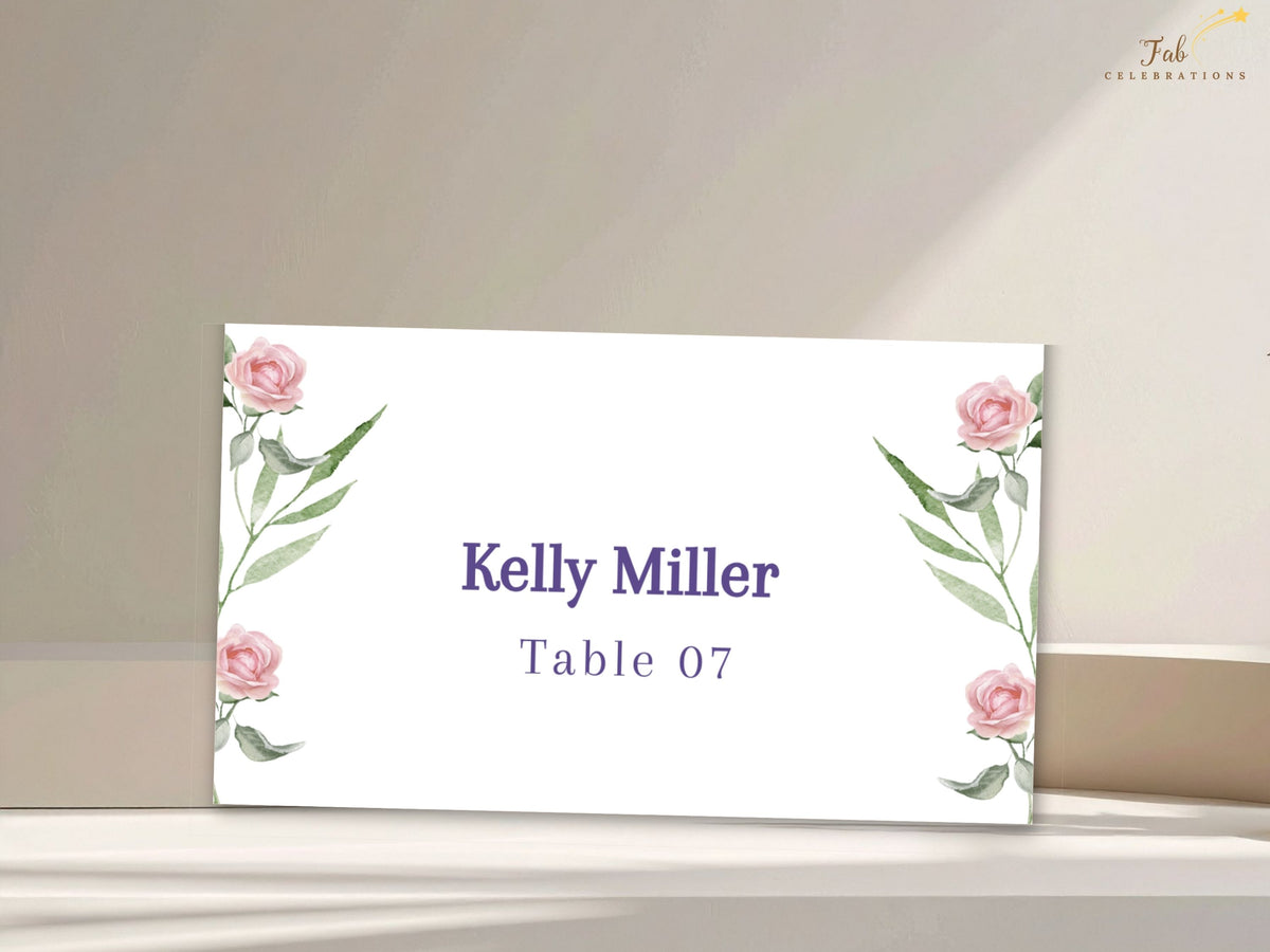 Botanical wedding place card featuring watercolor-inspired blush roses and delicate green foliage, with the guest name and table assignment arranged in refined purple type.