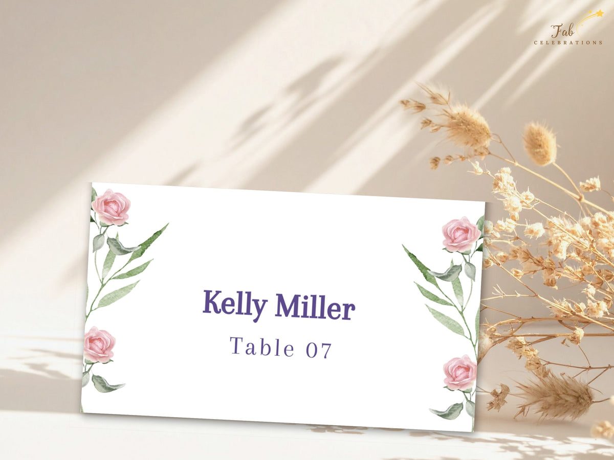 Elegant wedding place card decorated with watercolor-inspired pink roses and slender green foliage, with a personalized guest name and table number centered in purple typography.