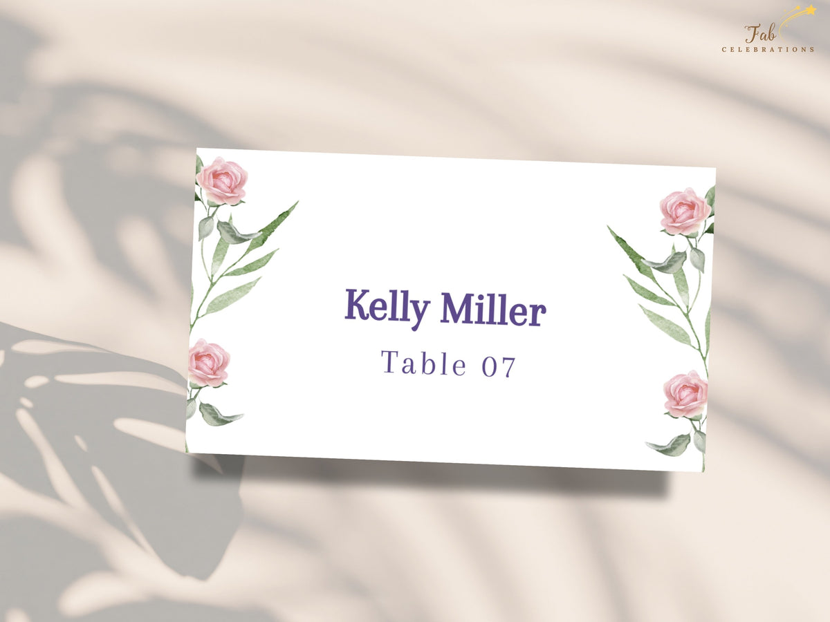 Wedding place card framed with watercolor-inspired pink roses and leafy green branches, displaying a personalized guest name and reception table number in a clean central layout.