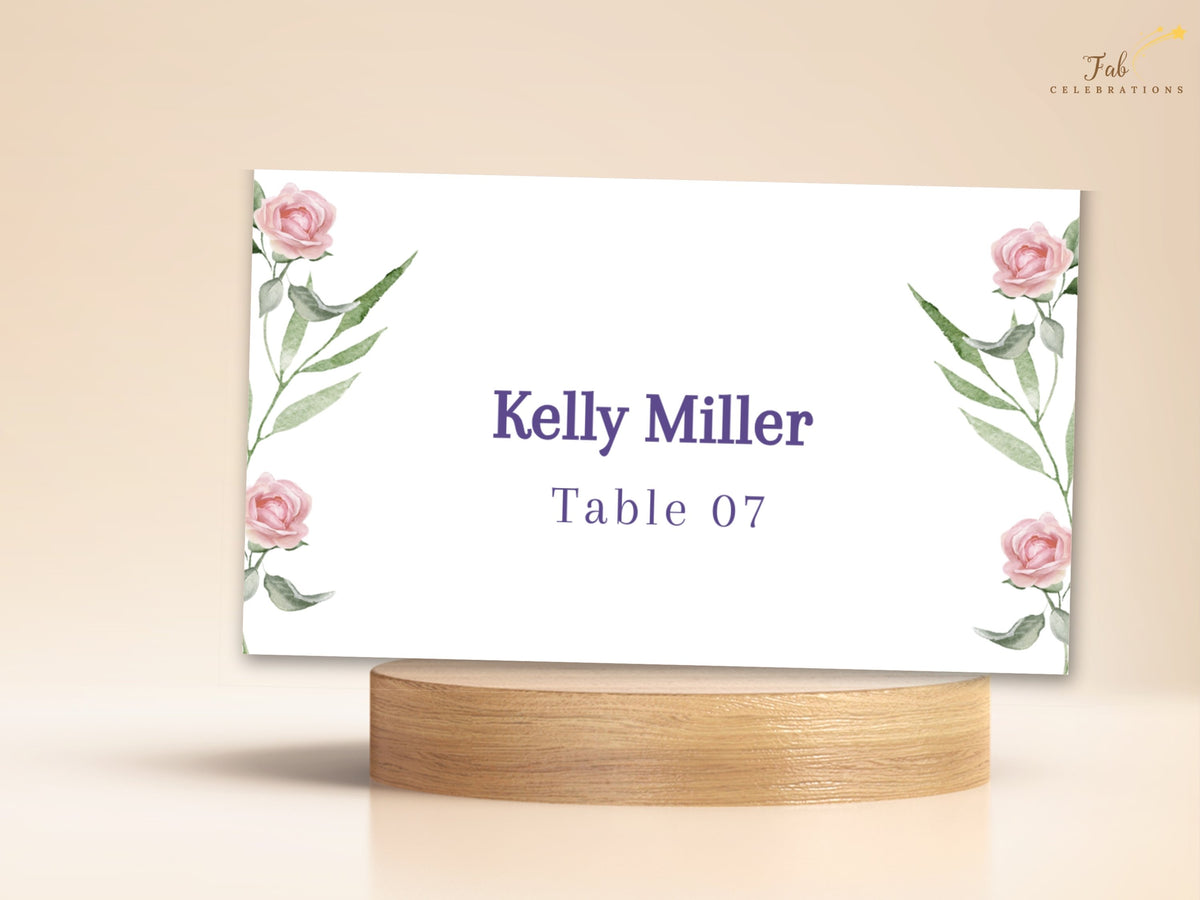 Wedding Place Card Template featuring watercolor-inspired blush pink roses and delicate green foliage framing the guest name and table number in elegant purple typography.