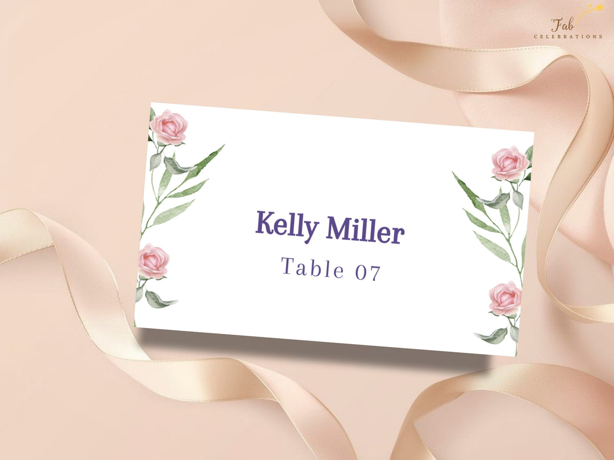 Wedding seating card featuring watercolor-inspired blush pink roses and airy green leaves, presenting the guest name and assigned table number in a clean romantic layout.