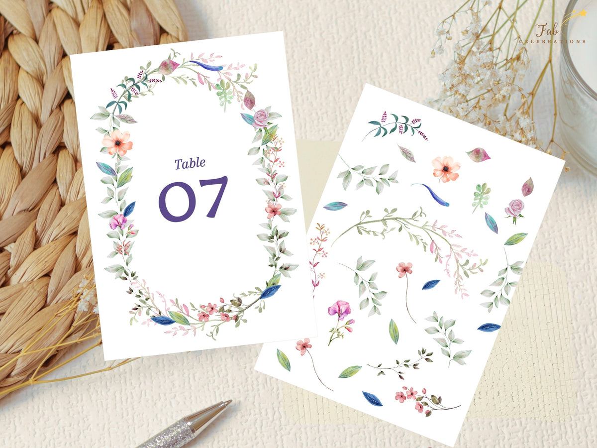 Wedding table number card displayed beside the coordinated watercolor-inspired floral artwork used to create its wreath of blossoms, leaves, and greenery.